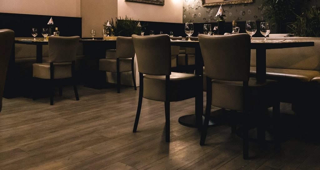 Dining room set for service: timber floor, upholstered chairs, wine glasses on dressed tables