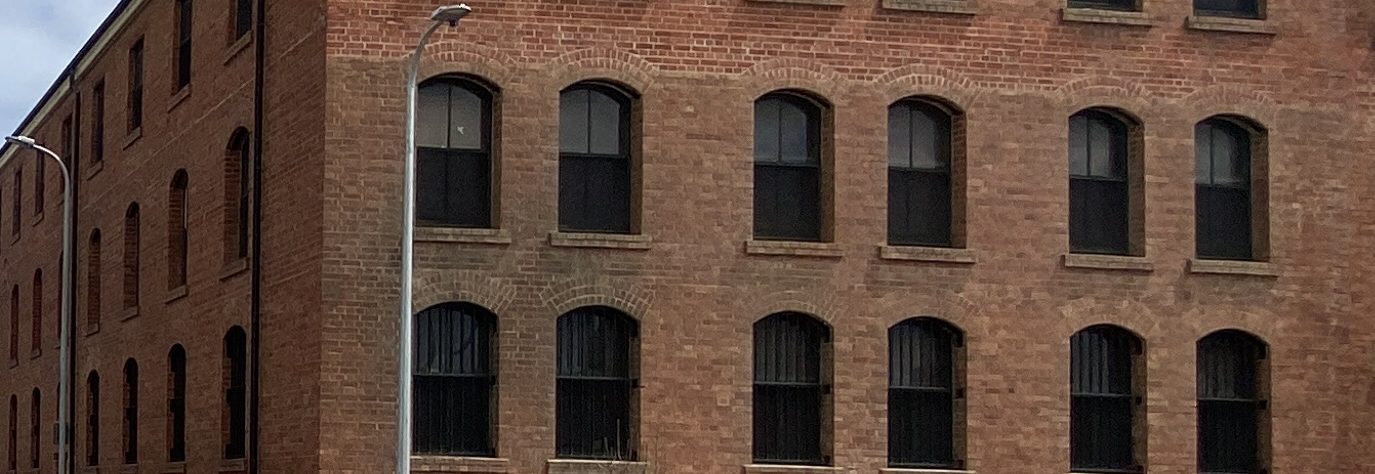 Four-storey nineteenth-century bond store in weathered brick, rows of arched windows across the frontage