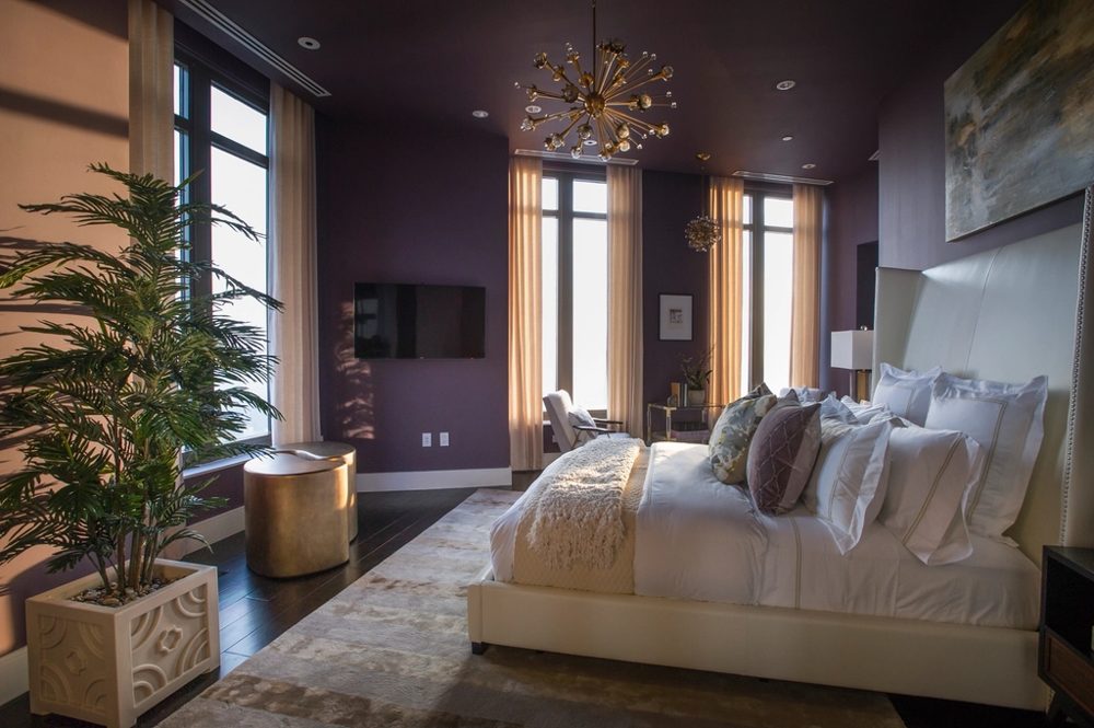 Corner guest room with a wide bed, pale linen, a potted palm and tall windows on two walls